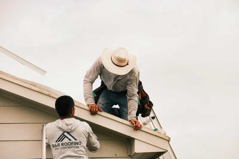 Two R&R Roofing crew members working along a roof eave