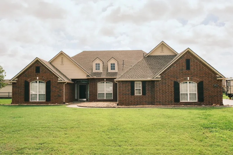 Brick home with a finished shingle roof seen across the front lawn