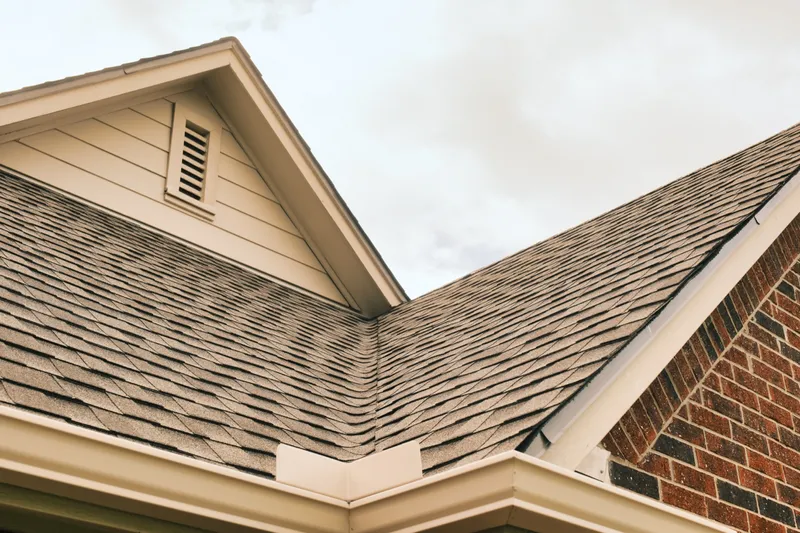 Completed shingle roof with a gable vent above brick and siding