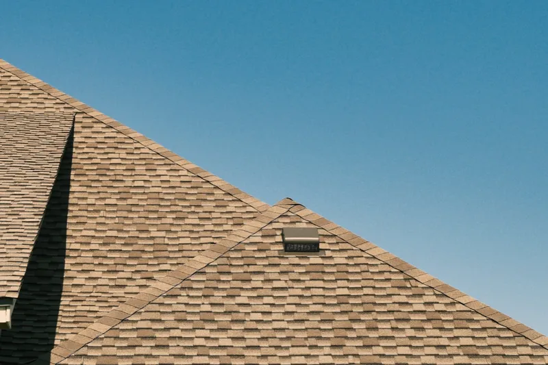 Completed shingle roof peak against a clear blue sky