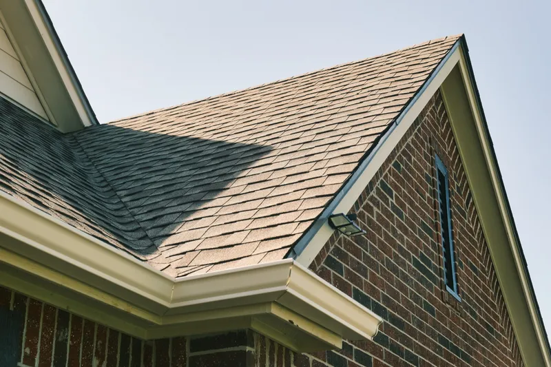 Close-up of a completed shingle roof and seamless gutter on a brick home