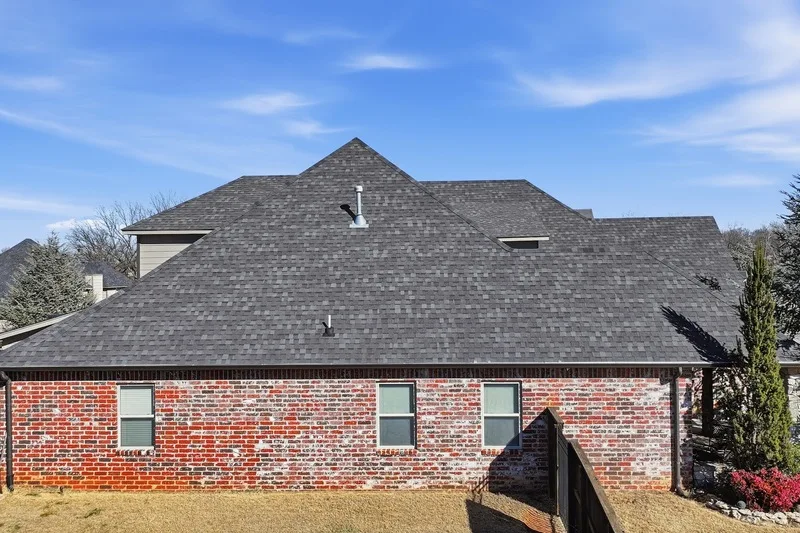 Finished shingle roof and hip line above a red brick home