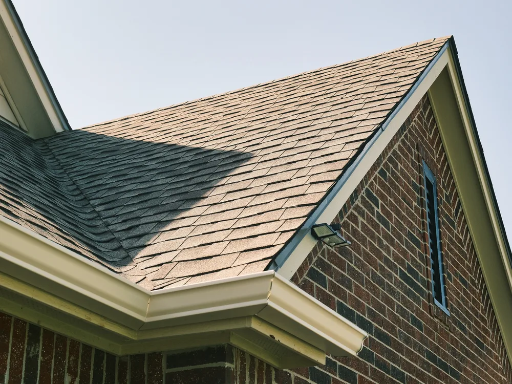 Close-up of a completed shingle roof and seamless gutter on a brick home