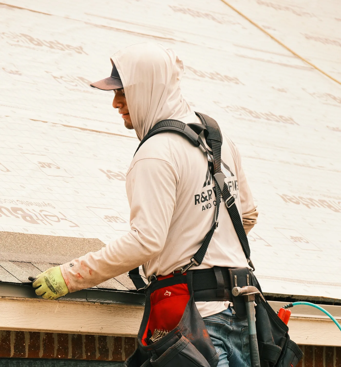 R&R Roofing crew member in a safety harness setting shingles along a roof edge