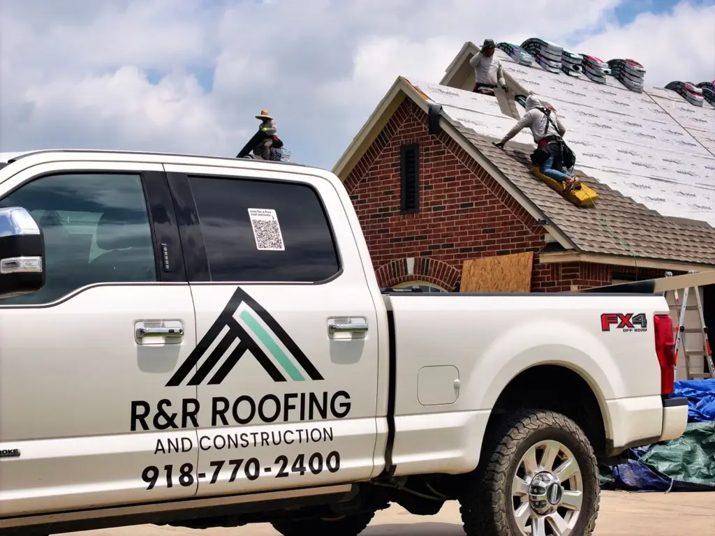 R&R Roofing and Construction truck parked at a job site while the crew installs new shingles on a brick home