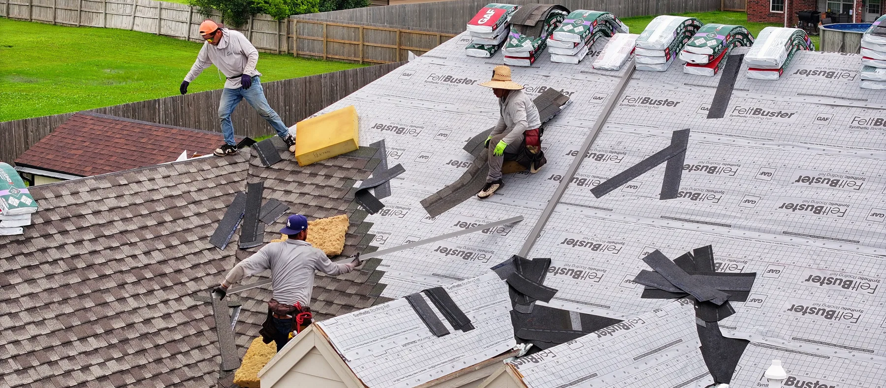 Aerial view of an R&R Roofing crew laying synthetic underlayment across a roof