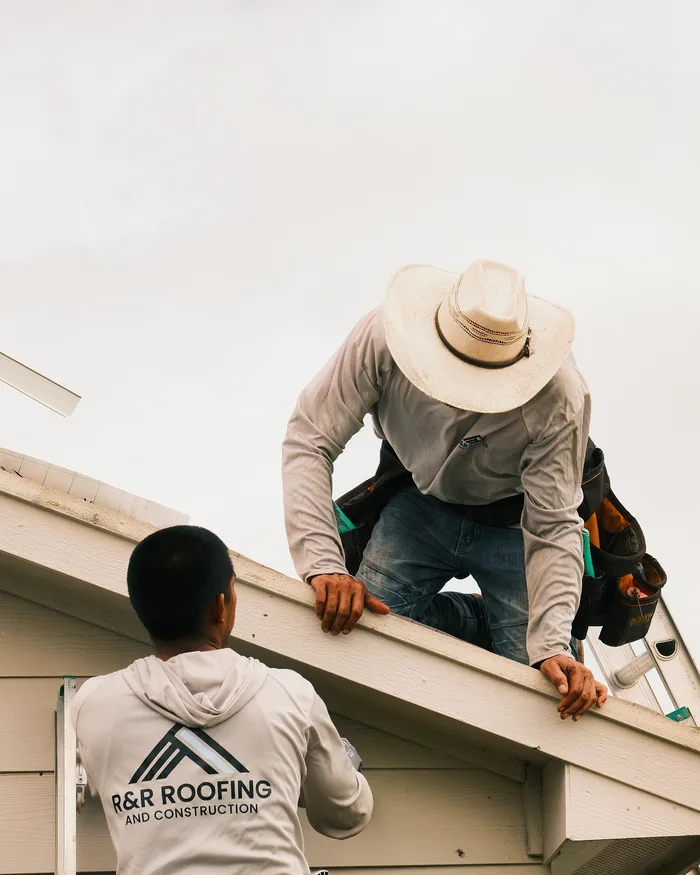 Two R&R Roofing crew members working along a roof eave
