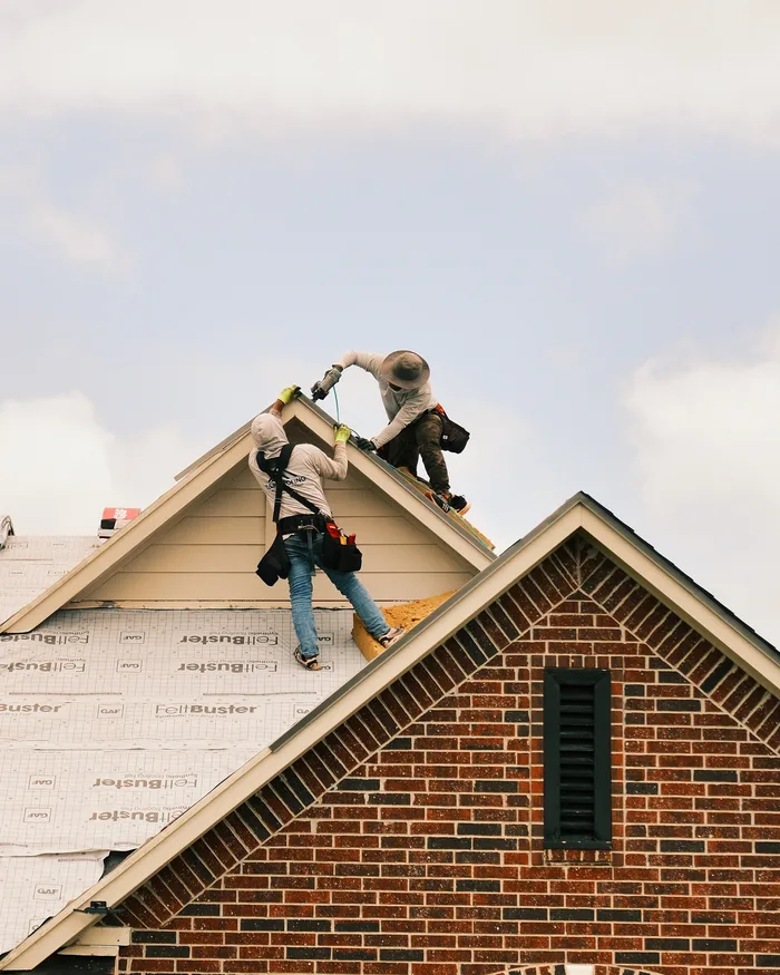 Two R&R Roofing crew members setting shingles along a roof ridge
