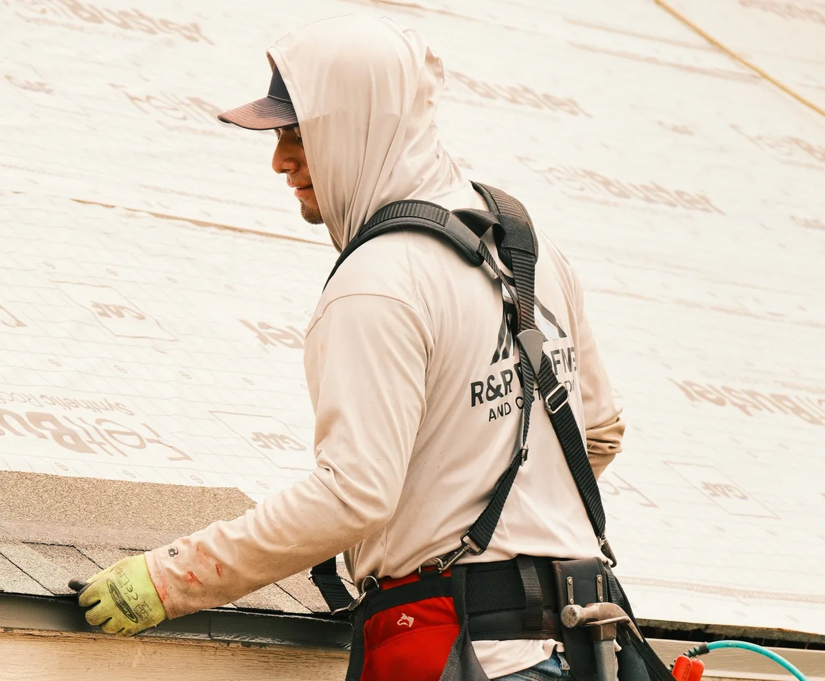 R&R Roofing crew member in a safety harness working along a roof edge over exposed underlayment